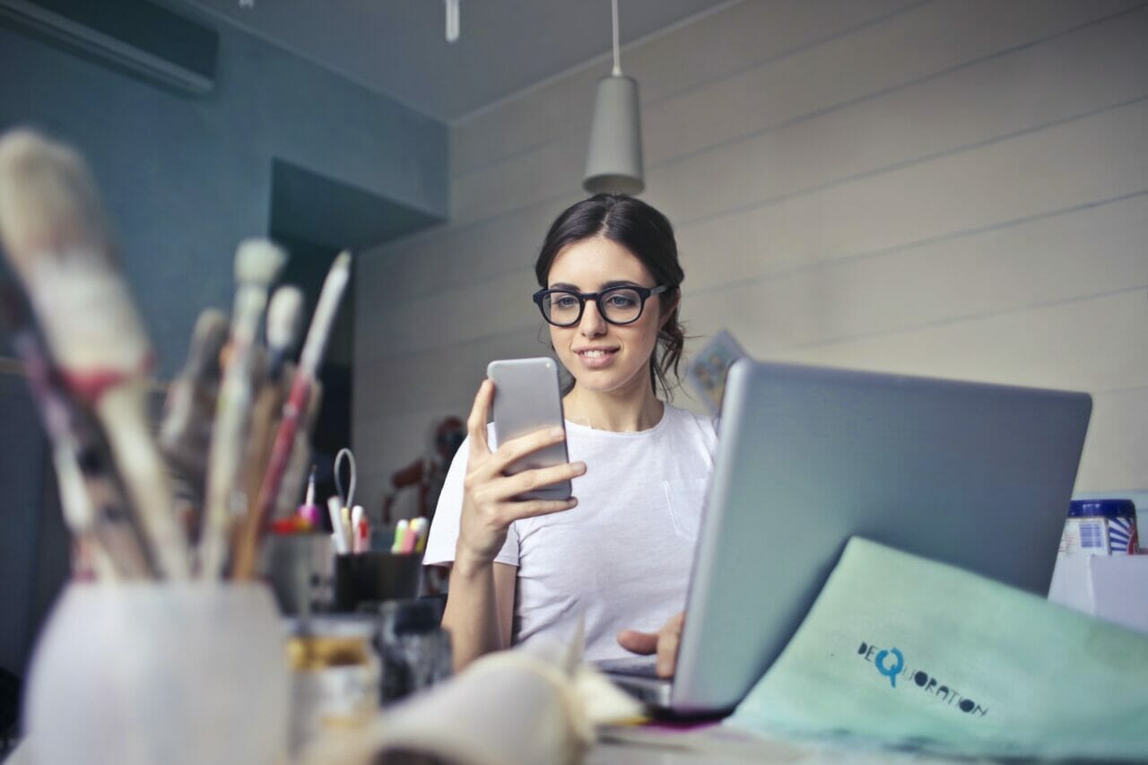 woman at busy desk reading feedback on her mobile phone